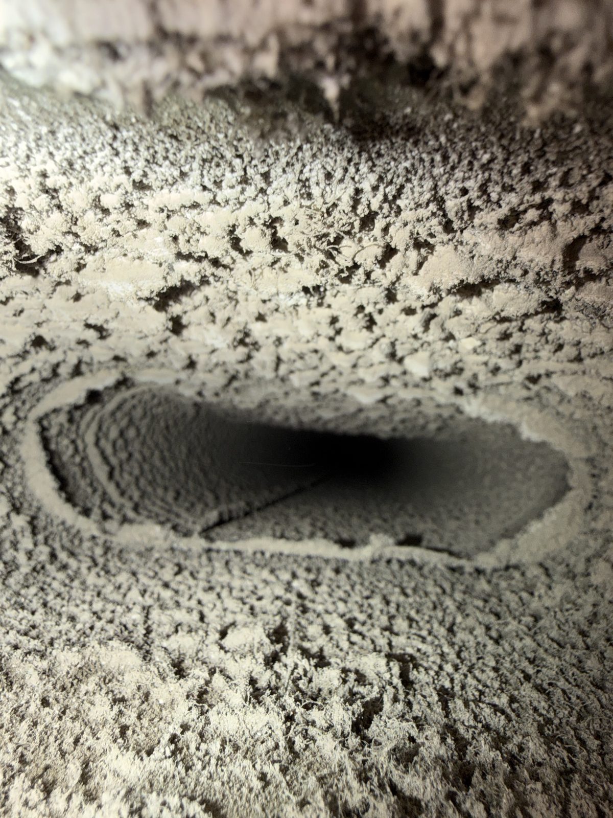 A duct floor carpeted in dust in front of an oval opening, before cleaning