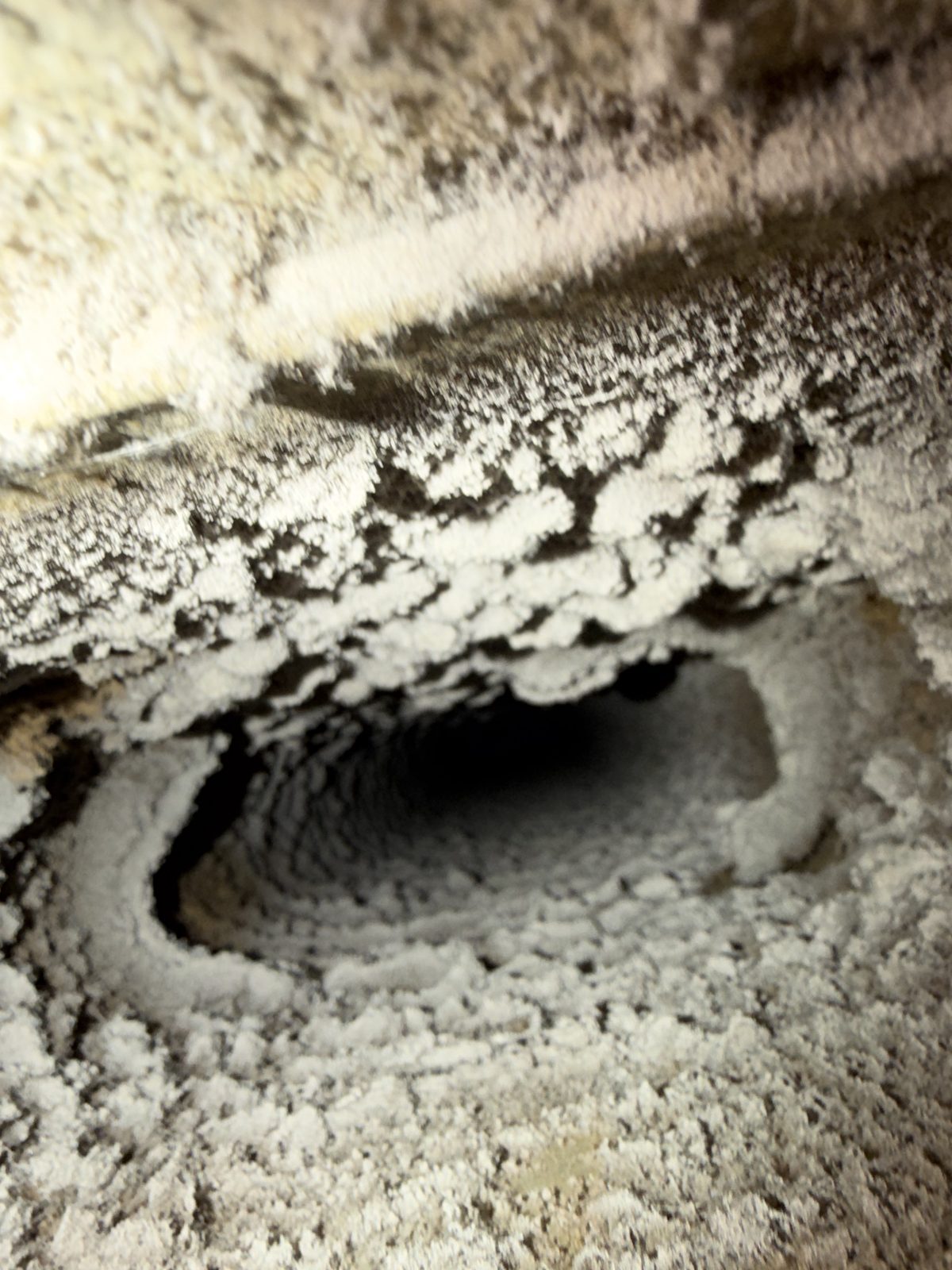 Dust built up thick around an oval takeoff inside a duct, before cleaning
