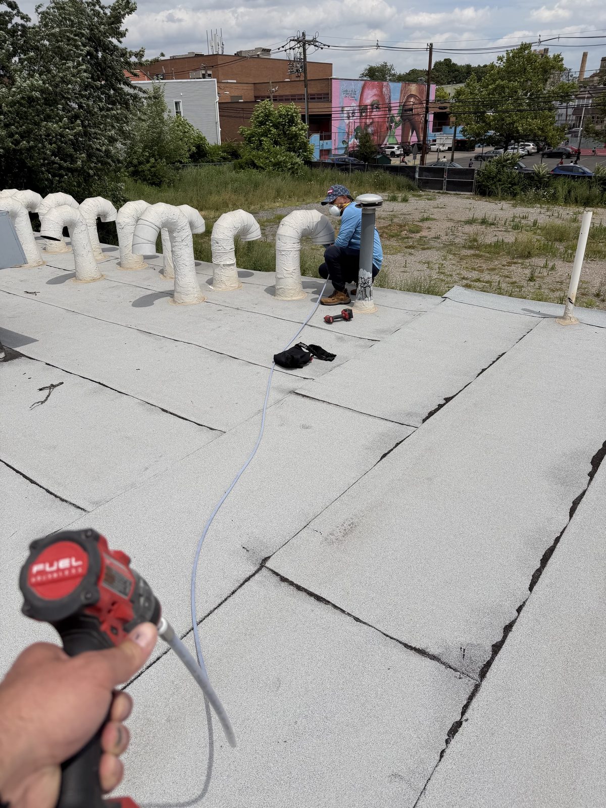 A row of gooseneck vents on a flat roof, an AMG technician at work at one of them