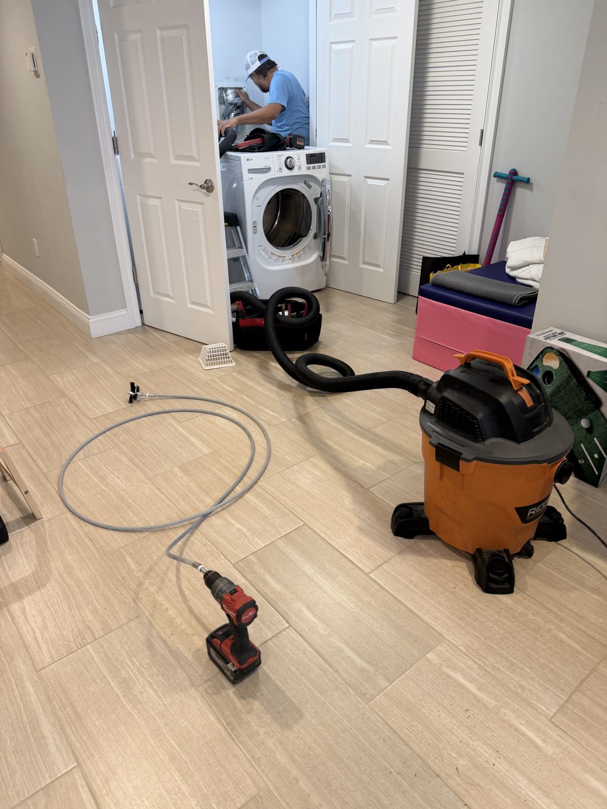 An AMG technician behind the dryer in a laundry closet, the vacuum and cleaning line on the floor