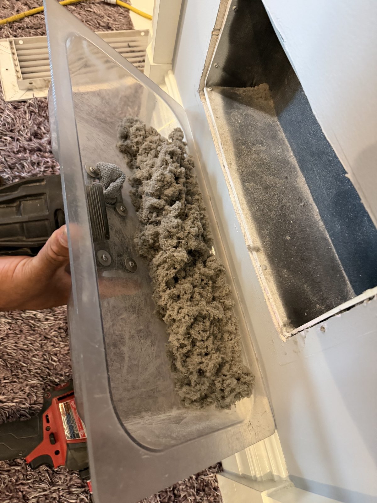 A clear catch tray held under a return opening, heaped with the dust and lint the brush pulled out
