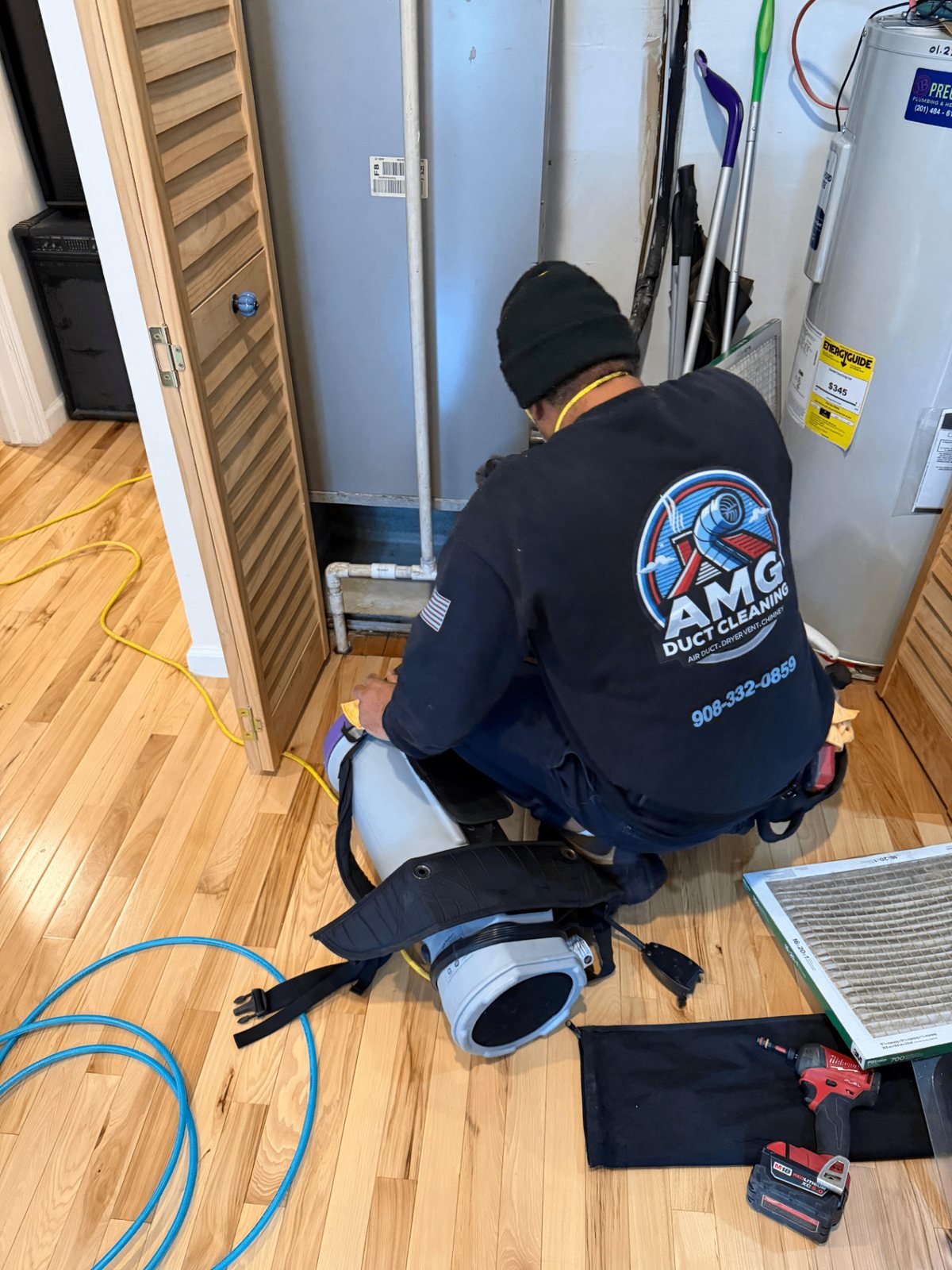 An AMG technician kneeling at a home's air handler with a portable vacuum, the old filter on the floor
