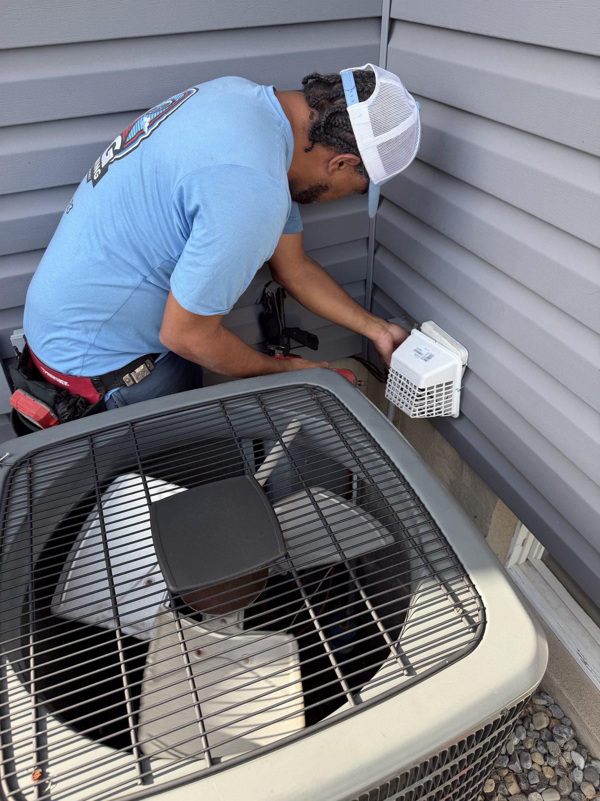 An AMG technician kneeling beside an air conditioning condenser to clean a dryer vent