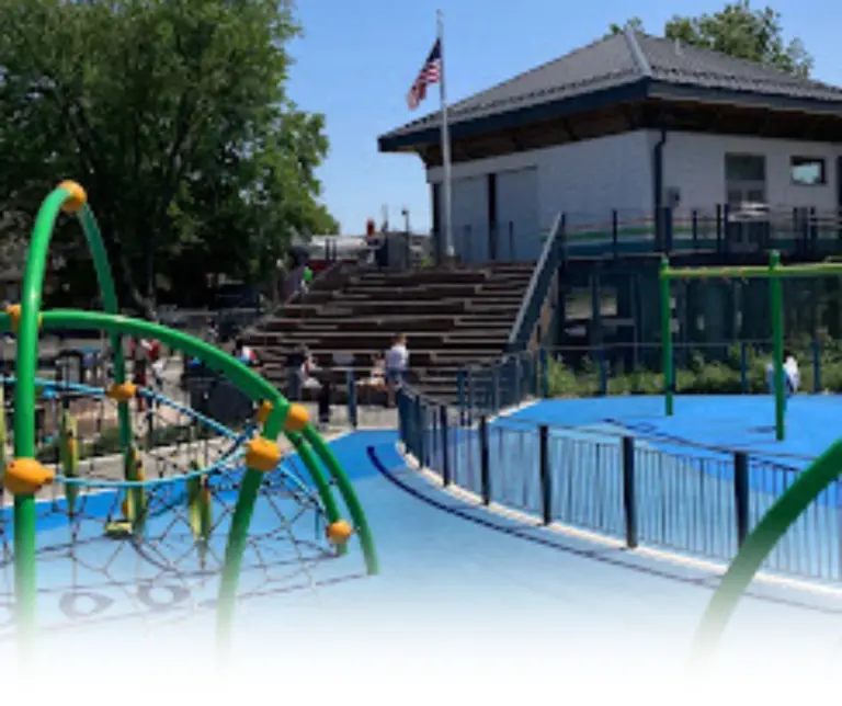 Playground area at Dundee Island Park with green climbing structures and a blue padded ground in Passaic County, NJ.