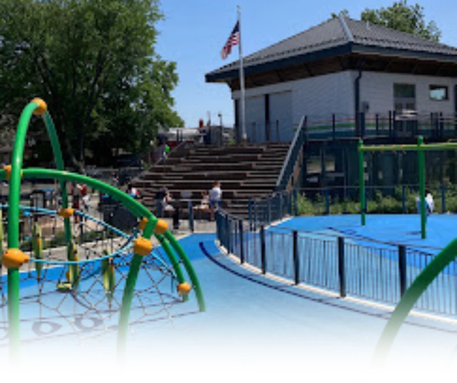 Playground area at Dundee Island Park with green climbing structures and a blue padded ground in Passaic County, NJ.